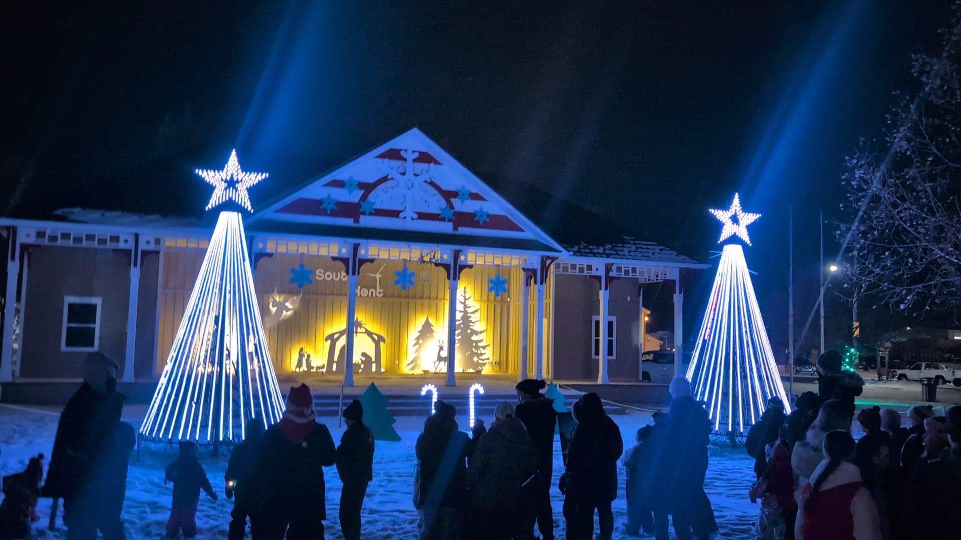 Crowd watching white pixel mega trees and searchlight beams at the park Christmas show